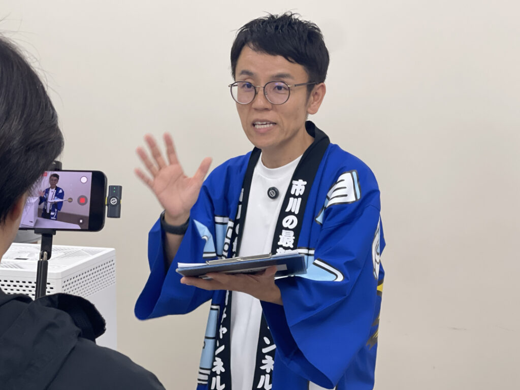 取材中、青い法被姿でカメラに向かって話す『女と男』の市川さん。